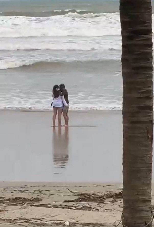 Dù trời âm u, nước biển đục ngầu và thỉnh thoảng có sóng lớn nhưng 2 người vẫn “bình chân như vại” tiếp tục nói chuyện hay ôm, hôn nhau. Họ không có vẻ vội vã hay hoảng sợ, lo ngại trước thời tiết bất thường này.