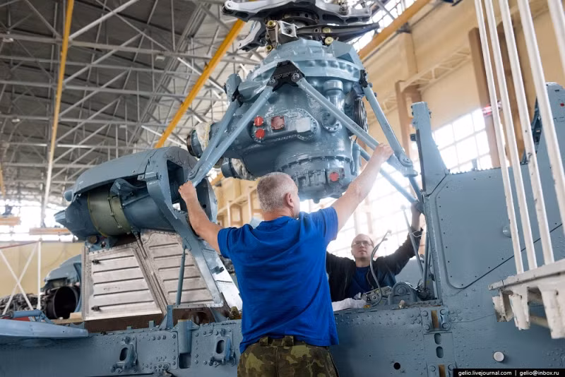 2 kỹ thuật viên đang điều chỉnh bộ phận truyền động cho rotor chính vào vị trí với sự trợ giúp của cần cẩu. Ảnh: Gelio.