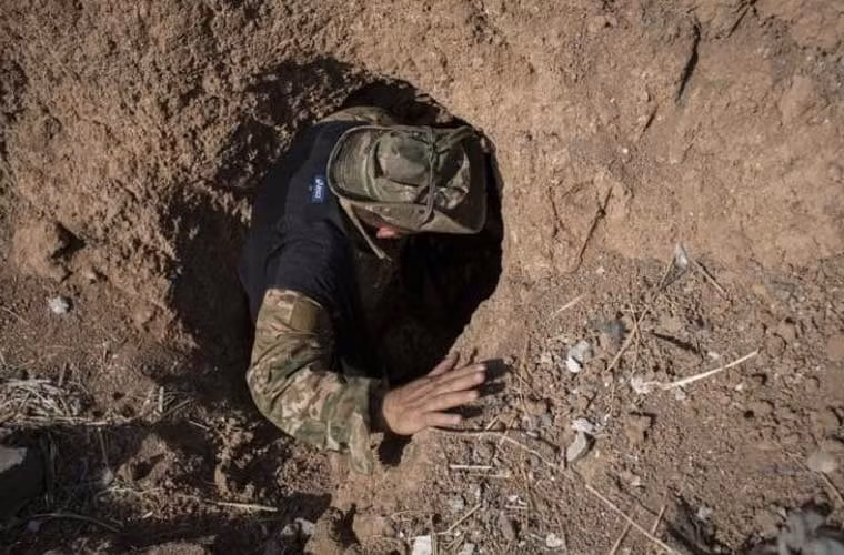 Một thành viên Peshmerga khảo sát hầm do IS đào ở làng. IS đã đào một đường hầm kéo dài 1 dặm kiểu thời Chiến tranh Thế giới 1 một bên làng. Trong khi đó, IS còn chúng còn đặt thuốc nổ TNT vào các bao cát đặt dọc hai bên con đường chính dẫn vào làng này.