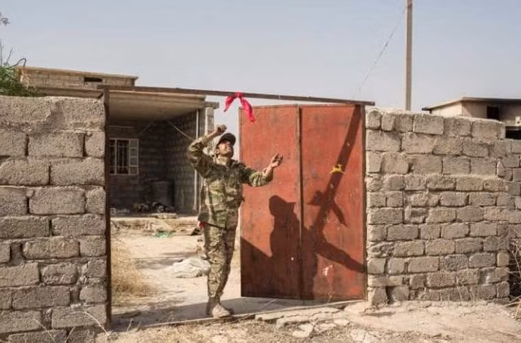 Một thành viên Peshmerga treo khăn đỏ bên ngoài một ngôi nhà để cảnh báo về các quả bom bị IS giấu trong nhà.