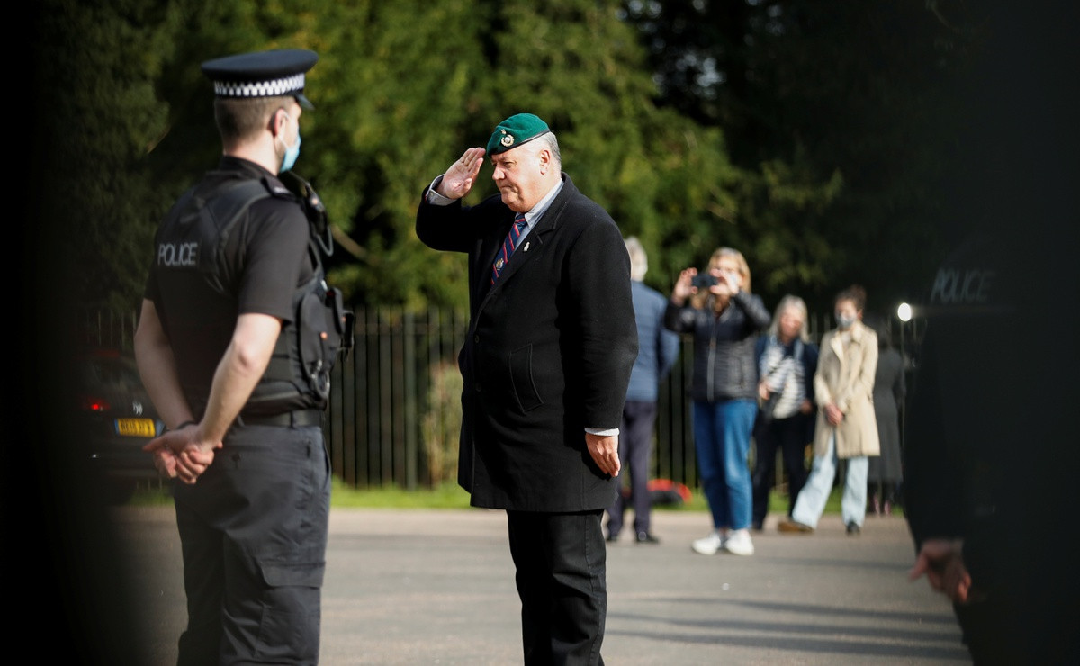 Một cựu quân nhân đứng nghiêm và chào kiểu nhà binh trước cung điện Windsor, trong khi nhiều người mang hoa đến để tưởng nhớ Hoàng thân Philip.