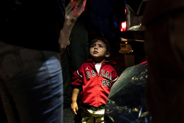 Một em nhỏ di cư nhìn về phía mẹ trong lúc chờ lực lượng tuần tra biên giới Mỹ đưa đi sau khi họ vượt sông Rio Grande vào Mỹ, tại Roma, bang Texas, hôm 5/4.