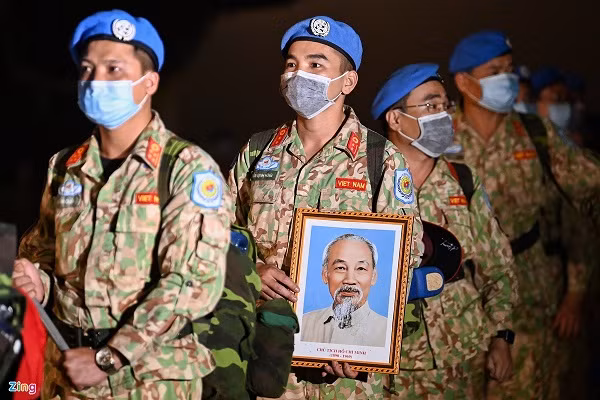 Ba người lính đi đầu mang theo cờ đỏ sao vàng, cờ của Liên Hợp Quốc và ảnh Bác Hồ. Trong số 38 cán bộ, chiến sĩ về đợt này, 32 người là y bác sĩ của Bệnh viện dã chiến cấp 2 số 2 kết thúc nhiệm vụ sau khi đổi quân với kíp Bệnh viện dã chiến cấp 2 số 3. 