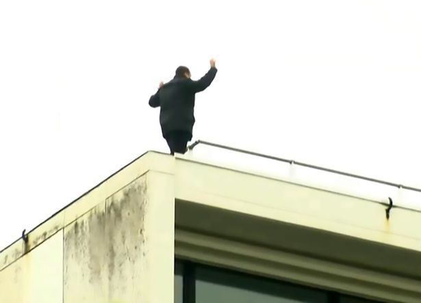 Kevin đứng trên nhà cao tầng khi bị cảnh sát vây ráp xung quanh.