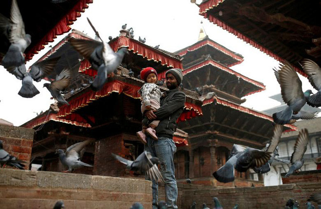 Người đàn ông bế con nhỏ, đứng xem chim bồ câu ăn trong một ngôi đền ở thành phố Kathmandu, Nepal. (Nguồn Guardian)