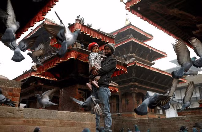 Người đàn ông bế con nhỏ, đứng xem chim bồ câu ăn trong một ngôi đền ở thành phố Kathmandu, Nepal. (Nguồn Guardian)