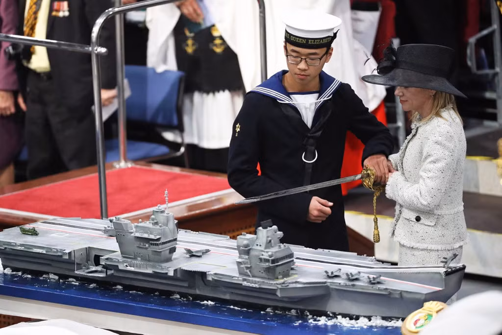 Steward Callum Hui, 17 tuổi, thủy thủ trẻ nhất trên tàu cùng với Karen Kyd, vợ của thuyền trưởng tiến hành nghi lễ cắt bánh mô hình của tàu. Đây là nghi thức truyền thống của Hải quân Hoàng gia Anh.