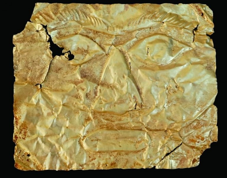 Mặt nạ vàng Giồng Lớn 2 cũng có hình chữ nhật. Phần mặt trước in nổi đôi mắt mở to, đôi lông mày cong cụp xuống cùng với sống mũi nổi cao, cánh mũi bầu. Góc dưới của má bên phải được thể hiện một hình gần giống mặt trời, với 1 vòng tròn ở giữa và nhiều tia xung quanh.