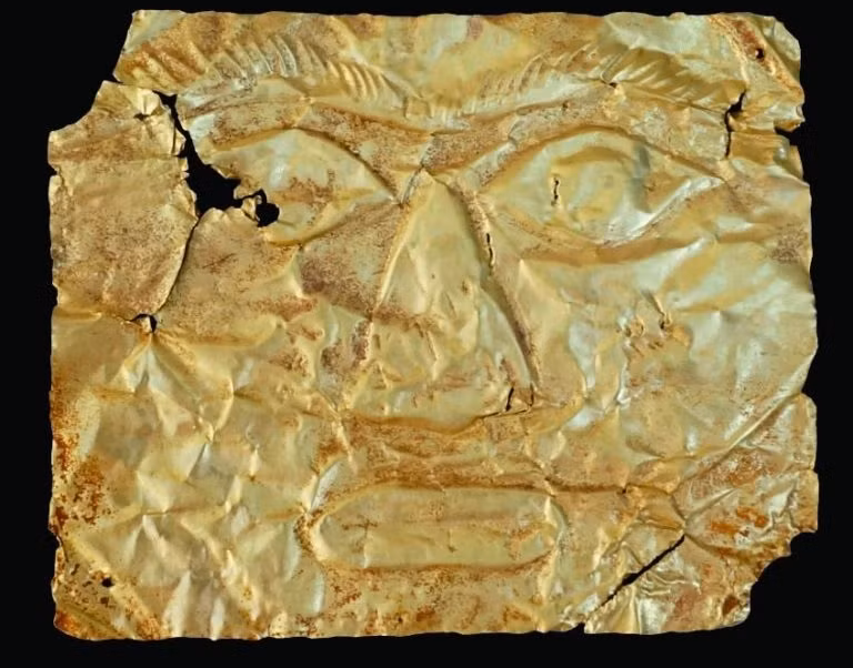 Mặt nạ vàng Giồng Lớn 2 cũng có hình chữ nhật. Phần mặt trước in nổi đôi mắt mở to, đôi lông mày cong cụp xuống cùng với sống mũi nổi cao, cánh mũi bầu. Góc dưới của má bên phải được thể hiện một hình gần giống mặt trời, với 1 vòng tròn ở giữa và nhiều tia xung quanh.