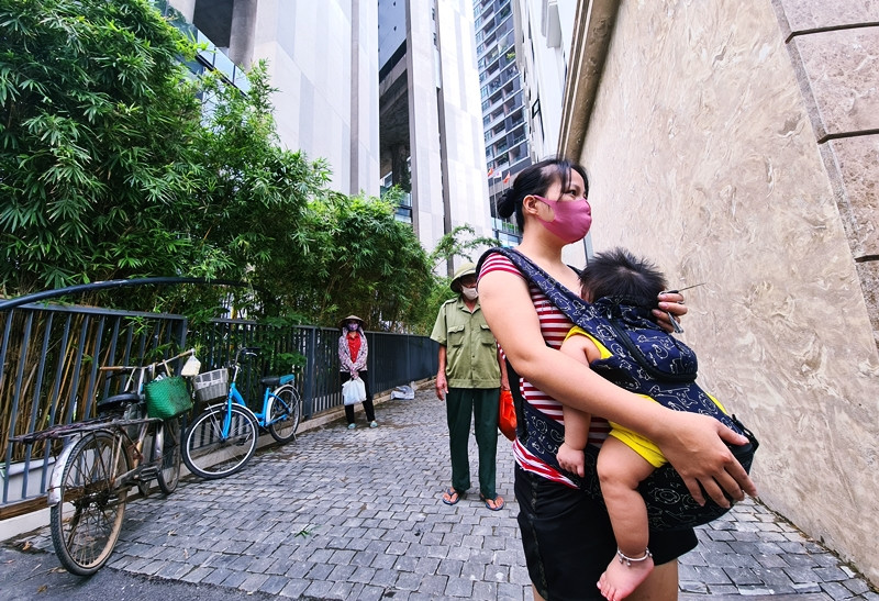 Người phụ nữ địu theo con nhỏ, kiên nhẫn xếp hàng chờ đợi đến lượt lên nhận gạo.