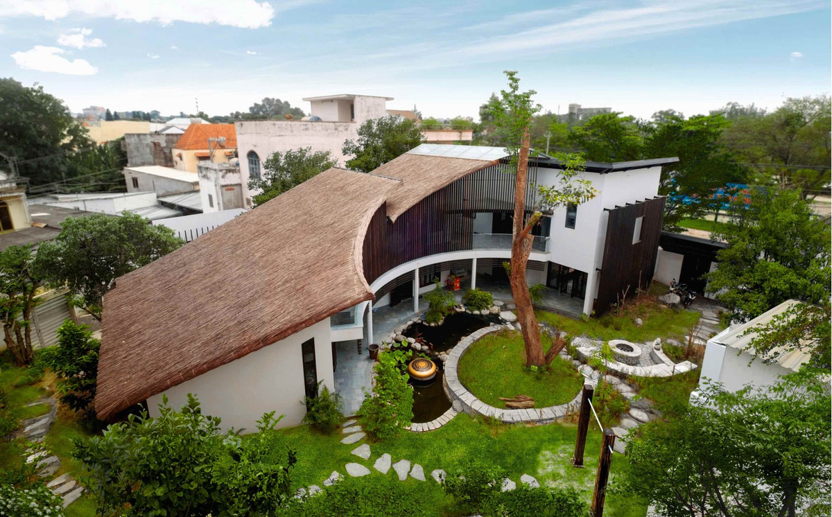 Nằm ngay trên trục đường lớn giữa thành phố Biên Hòa (Đồng Nai), ngôi biệt thự mang phong cách làng quê mộc mạc nổi bần bật với mái lá rộng và các khoảng hiên nép mình dưới tán cây. Ảnh: Sơn Vũ