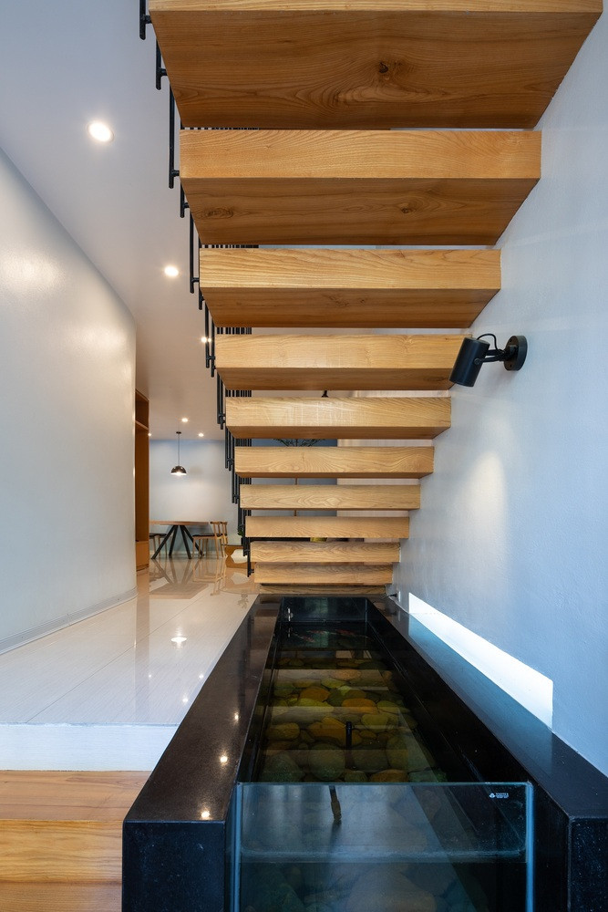 Gầm thang kết hợp làm lối vào phụ, bên dưới thiết kế bể cá nhỏ tạo cảnh quan sinh động. Ảnh: Triệu Chiến