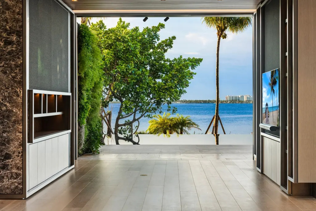 Phòng sinh hoạt ở tầng 1 có cửa kính từ sàn đến trần mở ra sàn gỗ và hồ bơi. Ảnh: Pagesix