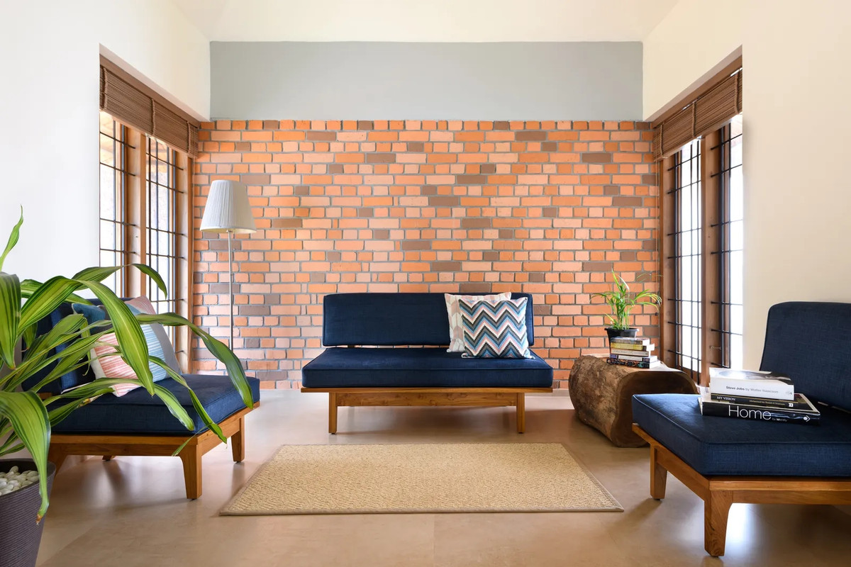 Nội thất trong nhà lấy cảm hứng từ đồng quê. Phòng khách nổi bật với bức tường gạch đỏ và ghế sofa màu xanh hải quân bắt mắt. Ảnh: Architecturaldigest