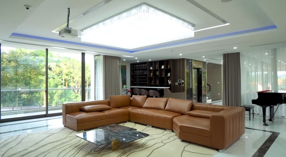 Phòng khách rộng mênh mông với sofa da và bàn mặt đá sang trọng. Ảnh chụp màn hình NhaTo