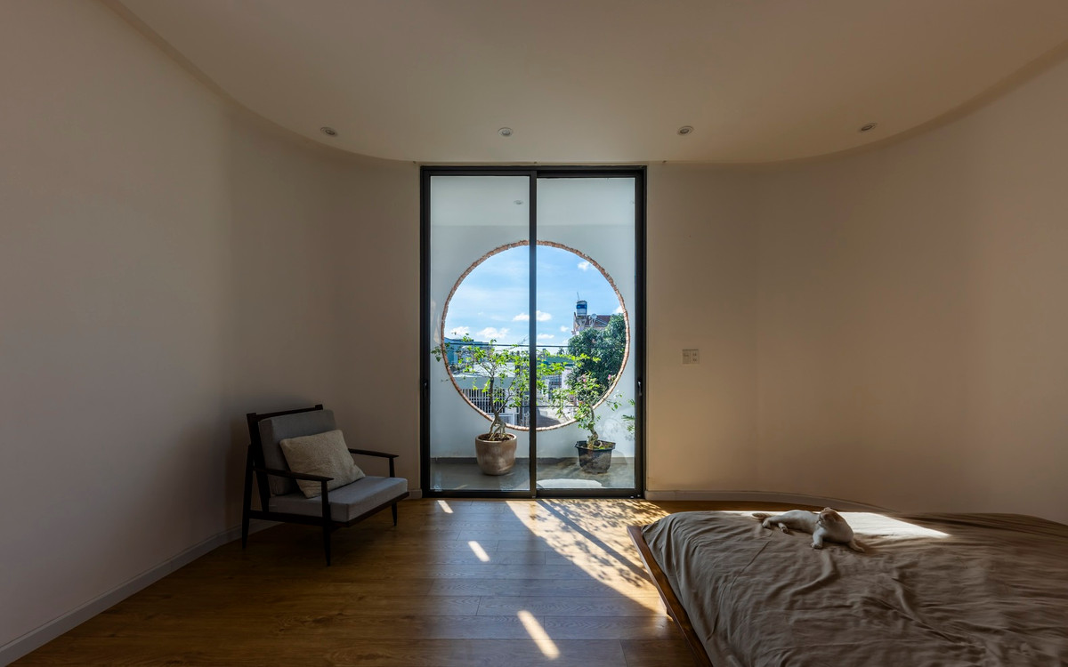 Phòng ngủ của bố mẹ được thiết kế theo phong cách tối giản, chú trọng vào sự thoải mái và yên tĩnh. Điểm nhấn của căn phòng là cửa sổ tròn lớn, mở ra tầm nhìn thoáng đãng. Ảnh: Hiroyuki Oki