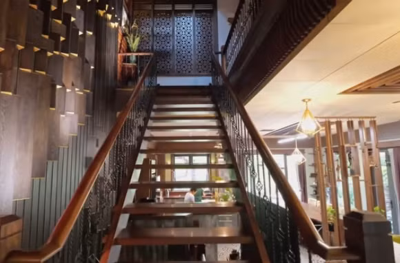 Cầu thang làm bằng gỗ lim Nam Phi. Đặc biệt, gia chủ đã mời các nghệ nhân từ Quảng Nam ra Hà Nội để thi công phần gỗ cho căn nhà và mất khoảng 2 năm mới hoàn thiện. Ảnh chụp màn hình NhaF