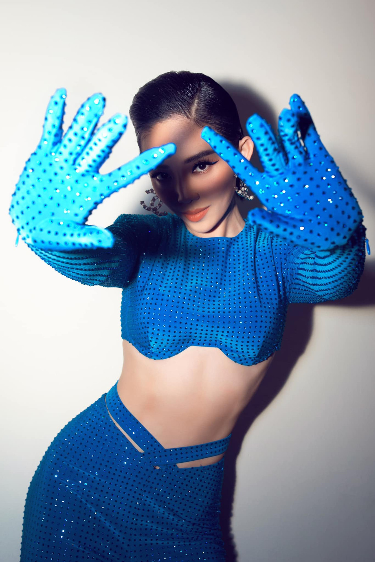 Vợ Hoàng Touliver nổi bật trong trang phục màu xanh lam, đính hạt lấp lánh phối kèm găng tay. Kiểu áo cut out táo bạo ôm sát phần thân trên giúp tôn vòng eo thon gọn của người đẹp.