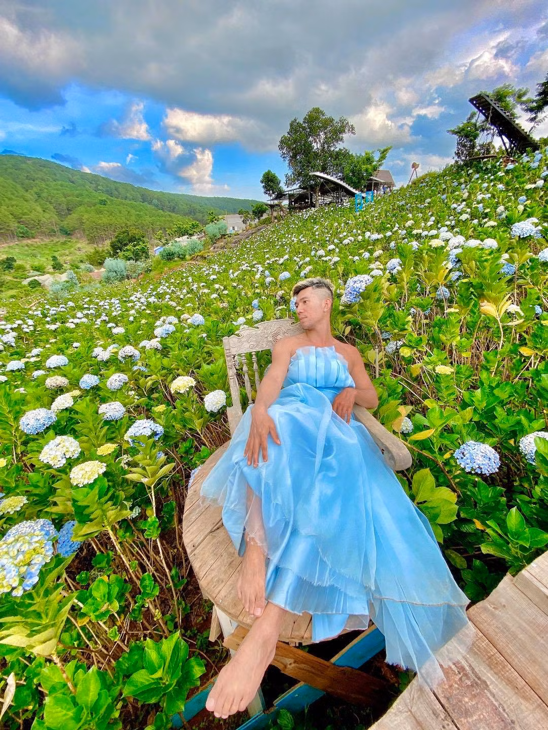 Nam nhạc sĩ diện chiếc đầm váy voan bồng bềnh, kiểu dáng cúp ngực tạo dáng lả lơi như thiếu nữ giữa cánh đồng hoa Cẩm Tú Cầu.