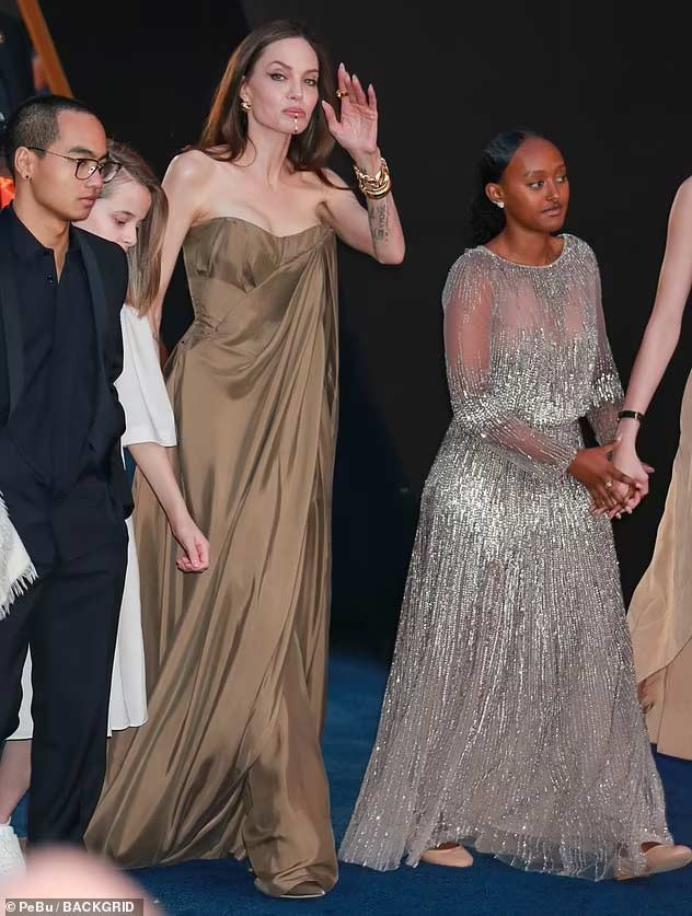 Zahara mặc váy của mẹ, nắm tay em gái Shiloh bước trên thảm xanh sự kiện công chiếu phim "Eternals". (Ảnh: Backgrid)