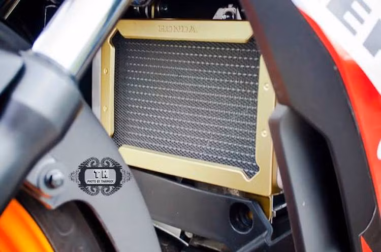 Ở phía sau bánh trước của chiếc xe, két tản nhiệt nguyên bản của Winner đã được bảo vệ bởi lưới chắn với khung màu vàng đẹp mắt. Đây là một trong các món phụ kiện được chính Honda thiết kế và sản xuất dành riêng cho Winner 150.