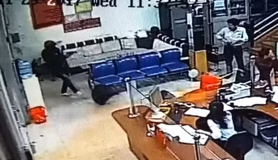 Thanh niên mặc đồ đen, kín mặt (trái) chĩa súng vào nhân viên bảo vệ, đồng thời đá túi vải về hướng nhân viên ngân hàng ý định cướp tiền - Ảnh cắt từ clip ngân hàng