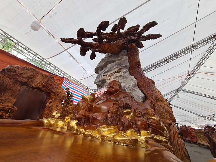 Chiếc bàn dài khoảng 4m, điểm nổi bật là hình Lân ở trước “cõng” trên lưng Phật Di Lặc đang ngồi dưới gốc cây tùng và cạnh một tảng đá lớn. Ngoài ra, xung quanh gốc cây được trang trí thêm những tiểu cảnh đá dát vàng 24k Đài Loan.