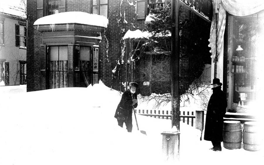 Một chủ cửa hàng đang xúc tuyết trên lối đi đến cửa hàng tạp hóa Boston Branch.