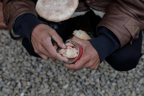 Một người nhập cư đang ăn bánh mì với đồ hộp.