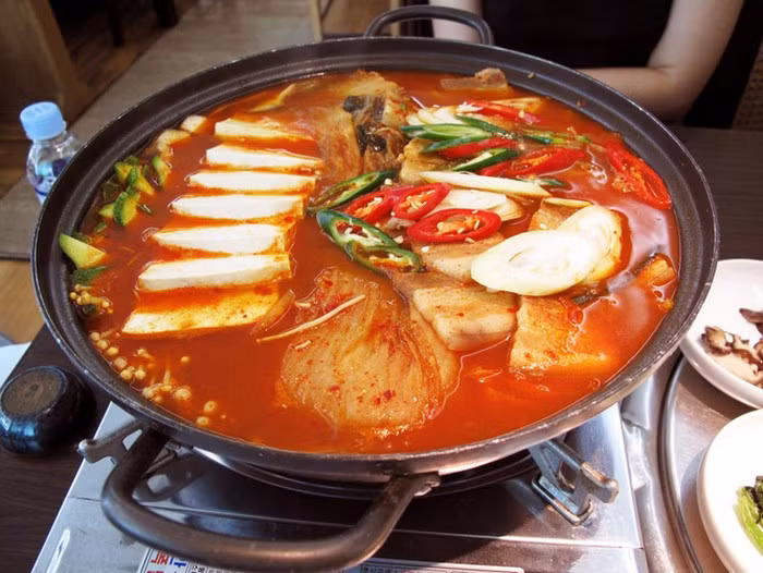 Thái kim chi thành khúc vừa ăn, đậu phụ thái miếng, hành tím băm nhuyễn, hành lá rửa sạch thái nhỏ. Phi thơm hành tím băm rồi cho thịt vào xào chín thì thả kim chi vào, đảo đều tay để kim chi ngấm dầu rồi đổ nước vào, xăm xắp mặt và tiếp tục đun. Nấu đến khi canh sôi chừng vài phút thì cho đậu non vào, đảo nhẹ tay để đậu không nát. Cuối cùng là thả hành lá vào rồi tắt bếp. Ảnh: Enbac.