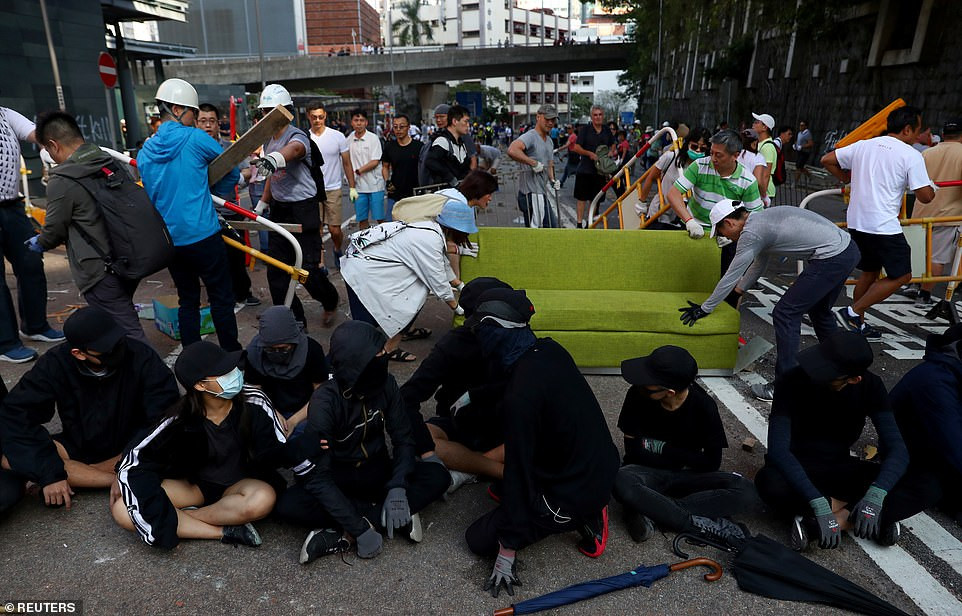 Vào tháng 10/2018, hơn 400 quân nhân được điều động đến các công viên của Hong Kong để hỗ trợ việc dọn dẹp cây cối gãy đổ, khắc phục hậu quả sau siêu bão Mangkhut. Ảnh: Người dân địa phương dọn dẹp chướng ngại vật trong khi một số người biểu tình ngồi trên đường bên ngoài Đại học Hong Kong ngày 16/11. 