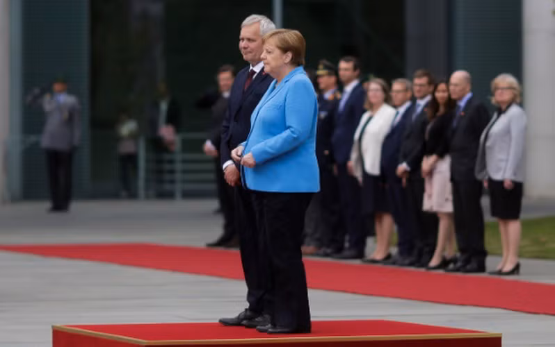Bà Merkel đã phải đổi tư thế từ buông thõng tay sang nắm hai tay lại với nhau nhưng vẫn không khống chế được cơn run rẩy. Chỉ khi bà bước đi, tình trạng run rẩy mới biến mất. Ảnh: Time.