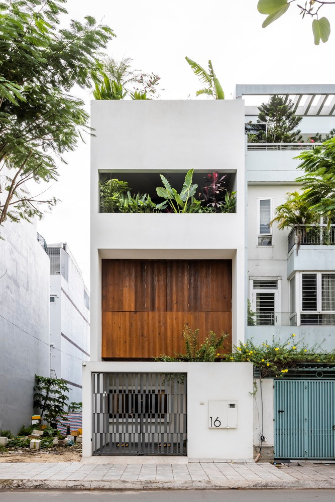 Mặt tiền ngôi nhà phố thiết kế tối giản. Những hình khối đặc – rỗng, được trung hòa bởi yếu tố tự nhiên như cửa gỗ và ban công trồng cây xanh.