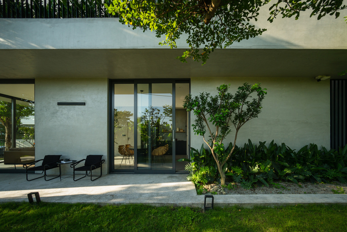 Tầng trệt được thiết kế là không gian giao tiếp linh hoạt bố trí dưới mái hiên rộng. Ban công rộng phía trên đóng vai trò như tấm vải sơn lớn che nắng, che mưa.