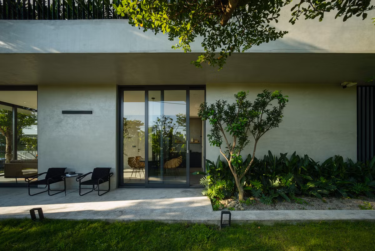 Tầng trệt được thiết kế là không gian giao tiếp linh hoạt bố trí dưới mái hiên rộng. Ban công rộng phía trên đóng vai trò như tấm vải sơn lớn che nắng, che mưa.