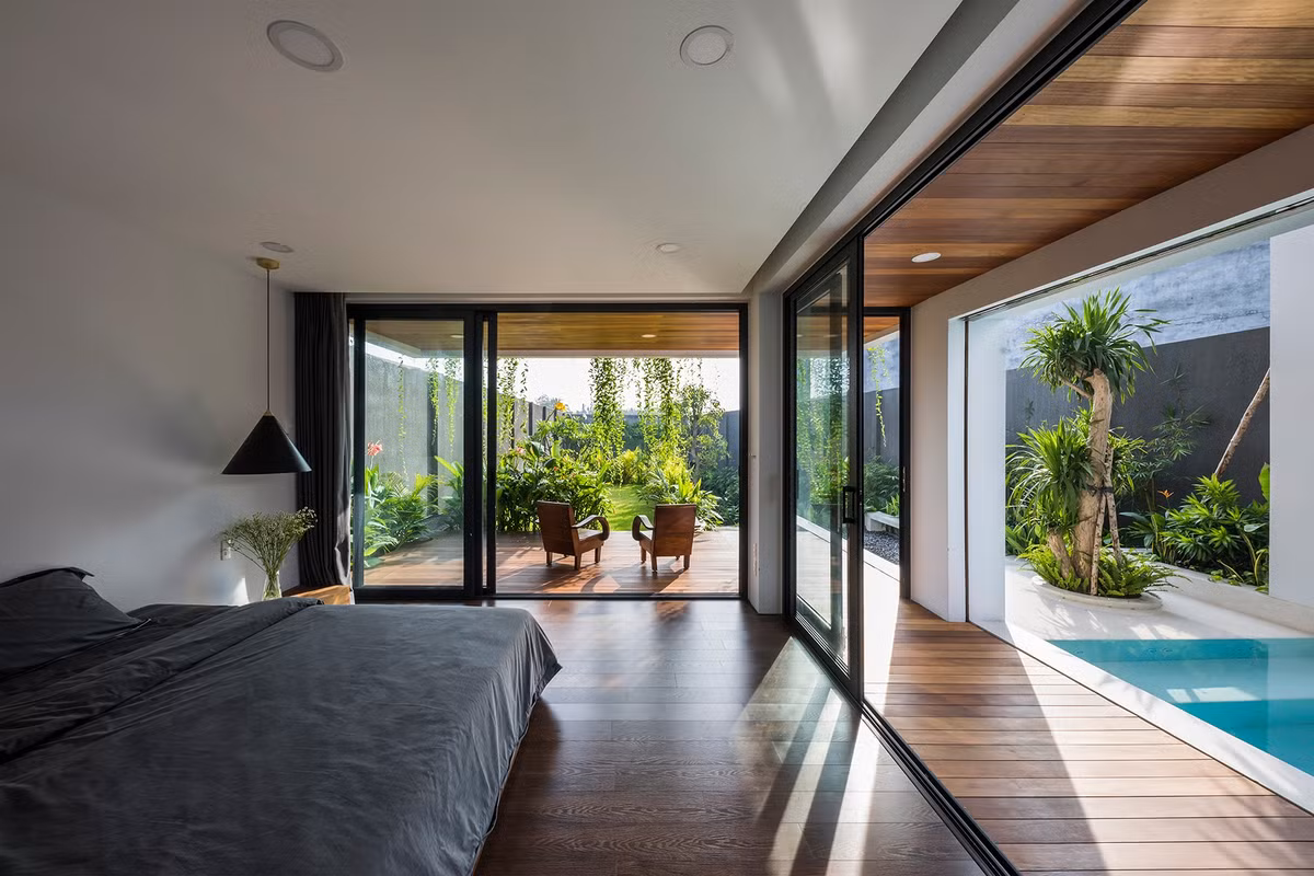 Phòng ngủ với lớp cửa kính lớn, nhìn ra bể bơi và sân chính.