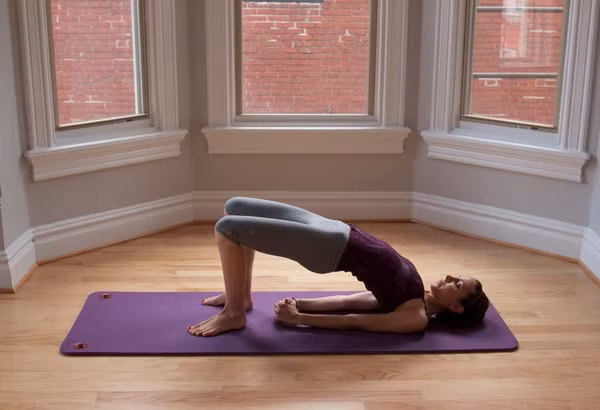 Giữ nguyên tư thế, hít vào, thở ra và hạ từng phần lưng xuống ( lưng trên, lưng dưới và lưng giữa). Lặp lại chuỗi động tác trong khoảng 6 – 8 nhịp thở, chỉ cử động khi thở ra. Sau khi kết thúc bài tập hãy kéo hai đầu gối về phía ngực và vòng tay ôm lấy gối. Thả lỏng hai vai. Đu đưa chậm rãi từ bên này sang bên kia và cảm nhận lưng bạn đang đè xuống sàn. Ảnh: Vietnamyoga.org.