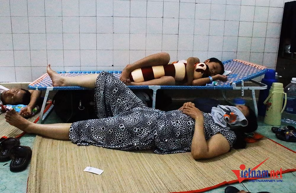 Phụ huynh cho con nằm trên chiếc giường gấp tự mua. Còn họ thì trải chiếu nằm dưới đất.