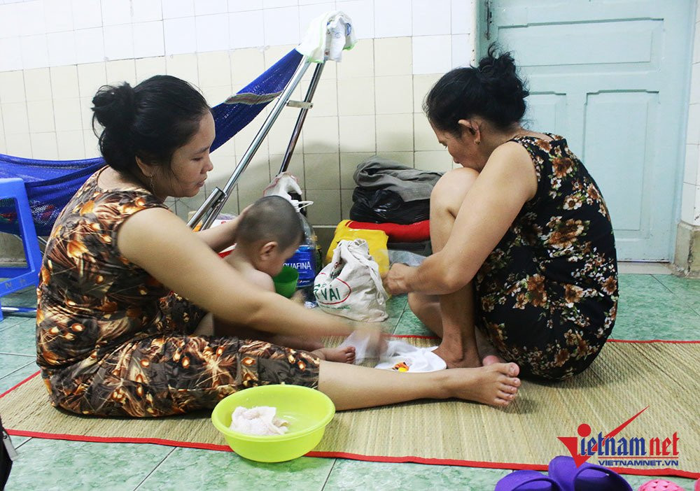 Chị Nguyễn Thị Thu Trang (Quận 2, TP.HCM) đang cho con tắm và thay quần áo. Chị cho biết, số lượng bệnh nhi đông nên mỗi giường bệnh nằm 2 bé. Ngoài ra, do thời tiết nắng nóng, chật chội nên gia đình chị phải chấp nhận mắc võng để cho con nằm ngủ ngoài hành lang.