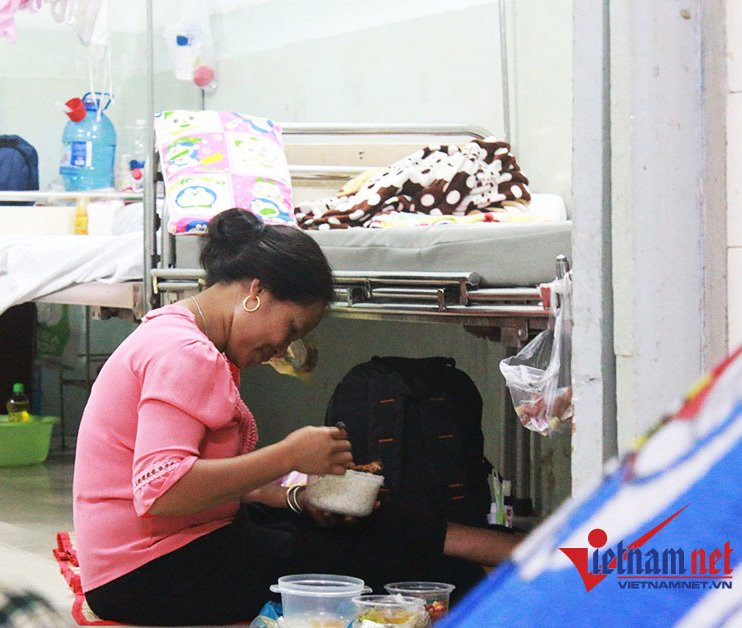 7 giờ tối, người nhà bệnh nhân ngồi dưới đất, cạnh gầm giường để ăn cơm.