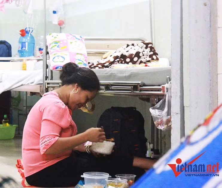 7 giờ tối, người nhà bệnh nhân ngồi dưới đất, cạnh gầm giường để ăn cơm.