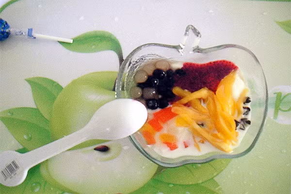 Sau khi đã sơ chế đầy đủ nguyên liệu thì chúng ta cho đá bào, hạt lựu, sữa chua, sữa đặc, mít vào bát. Rót thêm nước cốt dừa tạo hương vị, thạch màu, trân châu để thêm đẹp mắt và hấp dẫn hơn. Trộn đều là bạn đã có thể thưởng thức món sữa chua mít thơm ngon mát lạnh rồi. Ảnh: Douongonline.