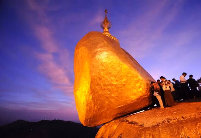 Người ta nói rằng, chùa được xây dựng trong thời gian Đức Phật còn sống, trên 2.500 năm trước. Nơi đây có một tảng đá thiêng, được bao bọc bởi những lá vàng dát mỏng, nằm cheo leo trên bờ một vách đá, được neo giữ chỉ bởi một sợi tóc của Đức Phật. Ngôi chùa được xây dựng trên tảng đá hình quả trứng to lớn đó trên độ cao 1100 m so với mặt biển. Gắn liền với hòn đá vàng là cả một truyền thuyết thú vị và kỳ bí về việc Đức Phật đến truyền đạo ở nơi đây. Bởi vậy, lúc nào nơi đây cũng có đông đảo người tới thăm viếng, chiêm bái, hành lễ. Một điều đặc biệt là mặt tiếp xúc giữa hòn đá và mặt đất chỉ có 78 cm².