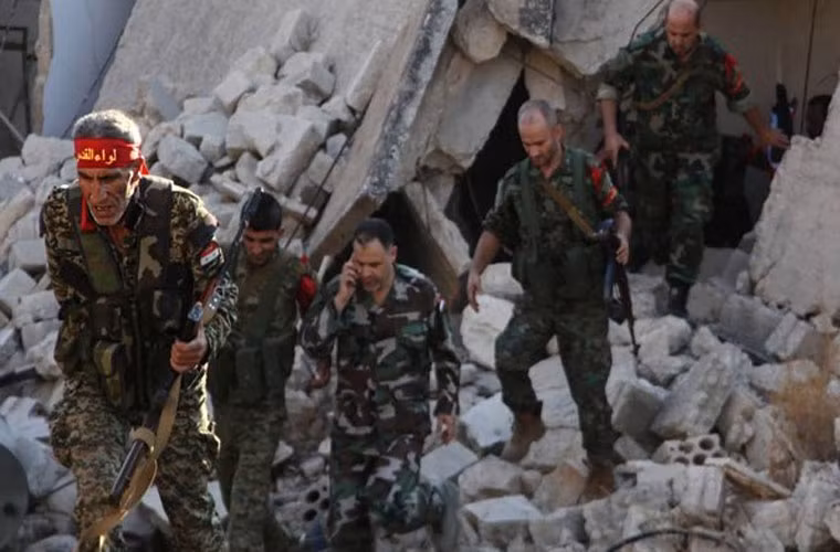 Các thành viên phe chính phủ Syria đi kiểm tra các tòa nhà bị tàn phá ở một khu dân cư mới được giải phóng. Ảnh FNA