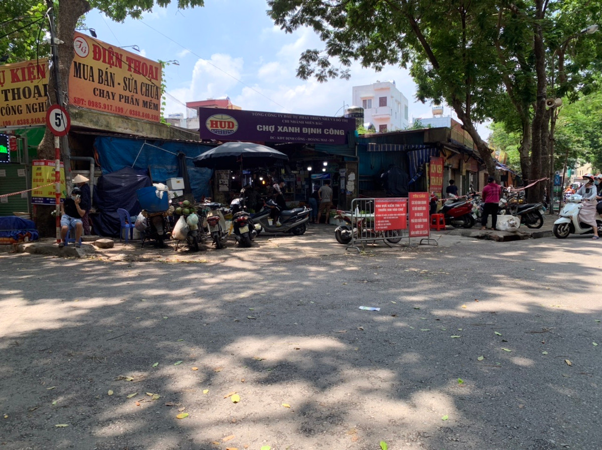 Chợ xanh Định Công (Hoàng Mai, Hà Nội) có lực lượng chức năng hướng dẫn người dân vào chợ mua hàng phải đảm bảo giãn cách. Các ki-ốt quanh chợ được căng dây đảm bảo giãn cách.