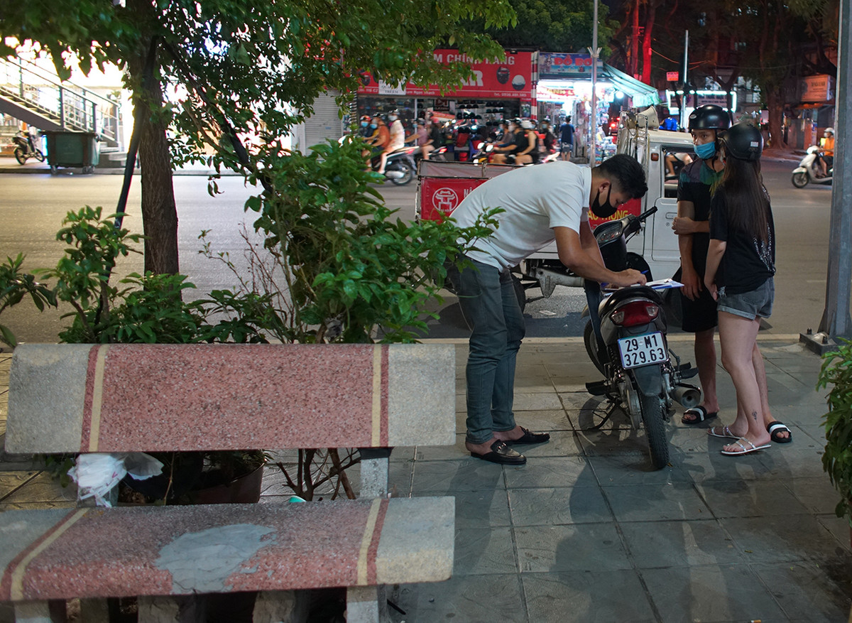 Cũng trong tối qua, lực lượng chức năng đã tiến hành xử phạt nhiều người về các lỗi vi phạm quy định phòng chống dịch COVID-19. Trong ảnh: Đôi bạn trẻ ngồi ghế đá không đeo khẩu trang bị Công an phường Kim Liên lập biên bản xử phạt 1 triệu đồng.