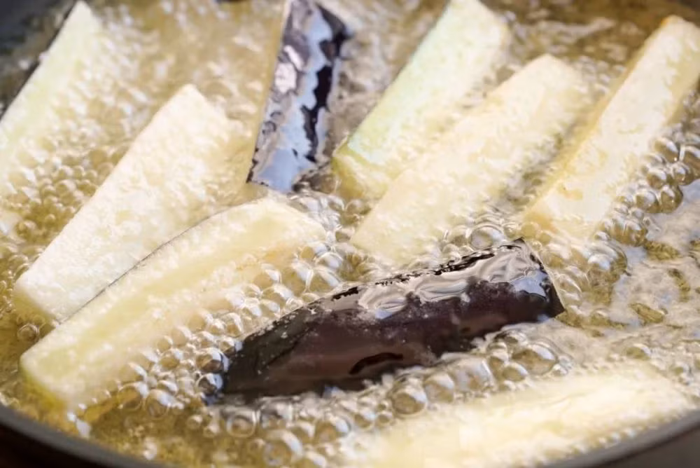 Tiếp theo cắt cà tím thành các dải dài và phủ một lớp tinh bột gạo lên trên. Đổ một lượng dầu ngập mặt cà, chiên cà tím đến khi chín vàng thì vớt ra.