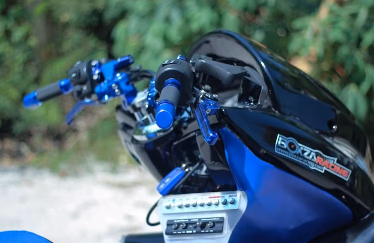 Thay vì ghi-đông nguyên bản, chiếc xe tay ga Honda PCX độ này đã được chủ xe thay tay lái bằng nhôm dạng clip-on của Bikers. Nằm phía trên tay lái là cặp tay phanh cũng của Bikers, bao tay Rizoma và gù xéo Rizoma - tất cả đều có màu xanh nổi bật. Phía trên tay lái là gương chiếu hậu Stealth nhỏ gọn.