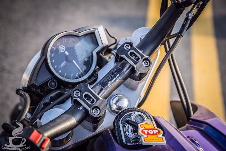 Với phuộc USD, chảng 3 trên dưới của xe cũng đã được thay thế. Nằm bên dưới cụm đồng hồ nguyên bản của FZ150i là ghi-đông nhôm nhuộm màu đen của hãng Dimotiv.