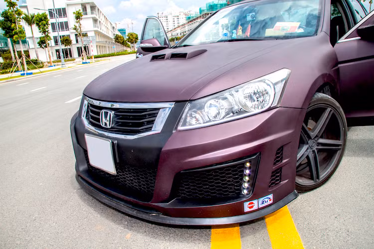 Trong đó, chi tiết nổi bật nhất trên chiếc xe phải kể tới bộ cản trước phong cách thể thao, được xưởng độ Phi Long tự thiết kế và gia công tại Việt Nam với các khe gió lớn đầy dữ dằn và hàng đèn LED hai bên. Ở phía trên nắp ca-pô, chiếc Accord cũng được "trổ" thêm khe gió làm mát theo phong cách xe "cơ bắp" Mỹ.
